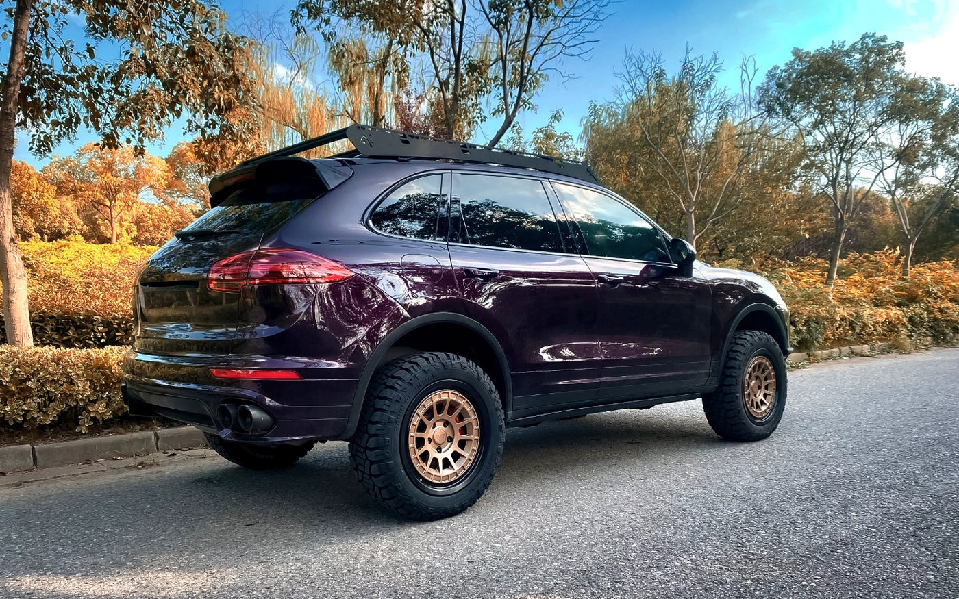 Purple Lifted Porsche Cayenne 958 with off-road tires on a road surrounded by trees and foliag