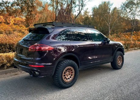 Purple Porsche Cayenne 958 turbo S overland build with off-road tires on a road surrounded by trees with autumn foliage.