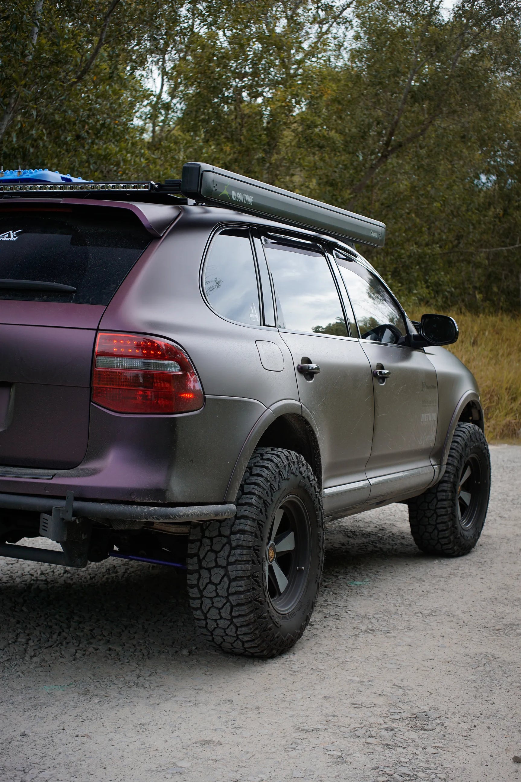 Purple Porsche Cayenne 957 overland with off-road tires and roof rack on a dirt road