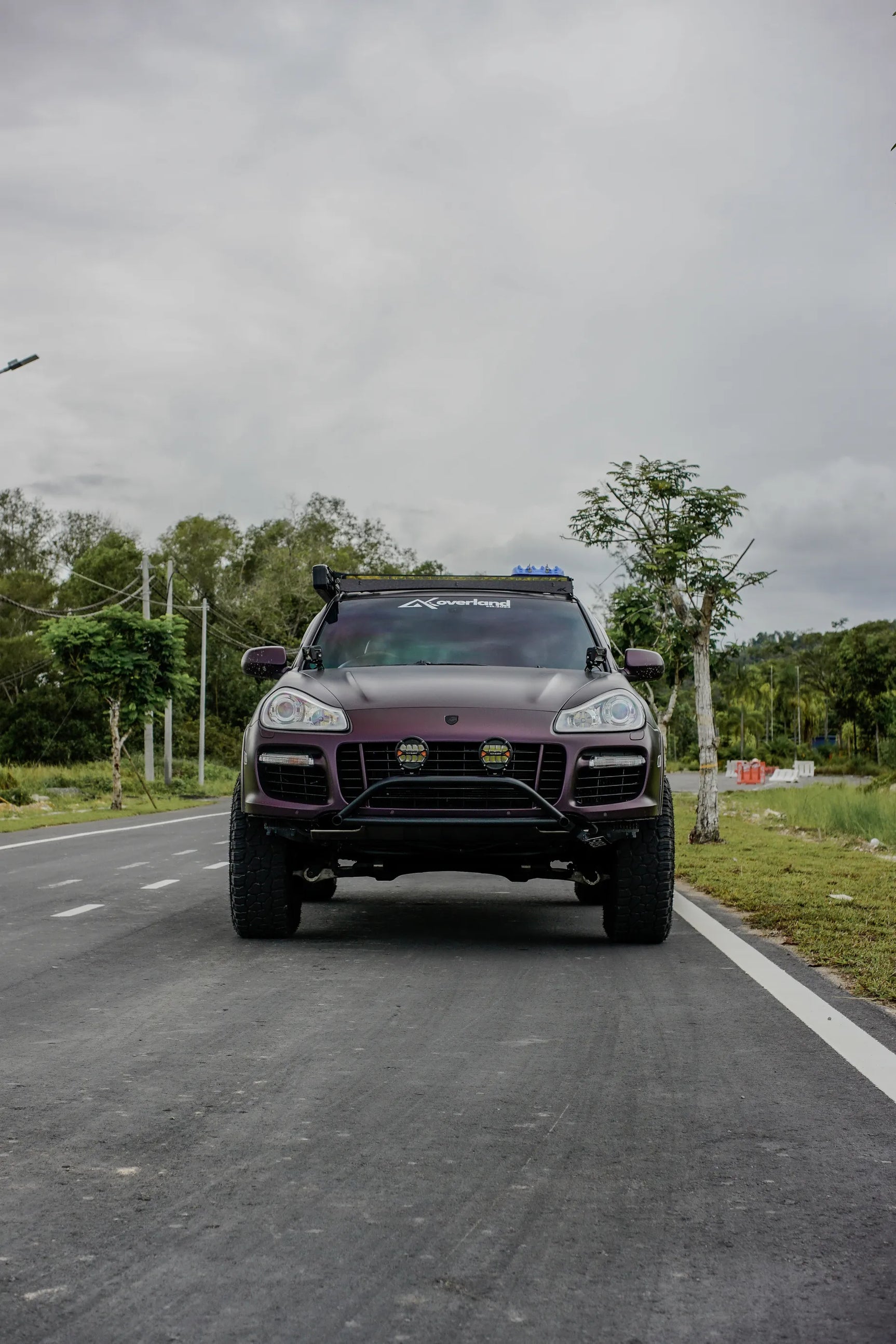 Purple Porsche Cayenne 957 overland with off-road tires and roof rack with novsight led driving lights