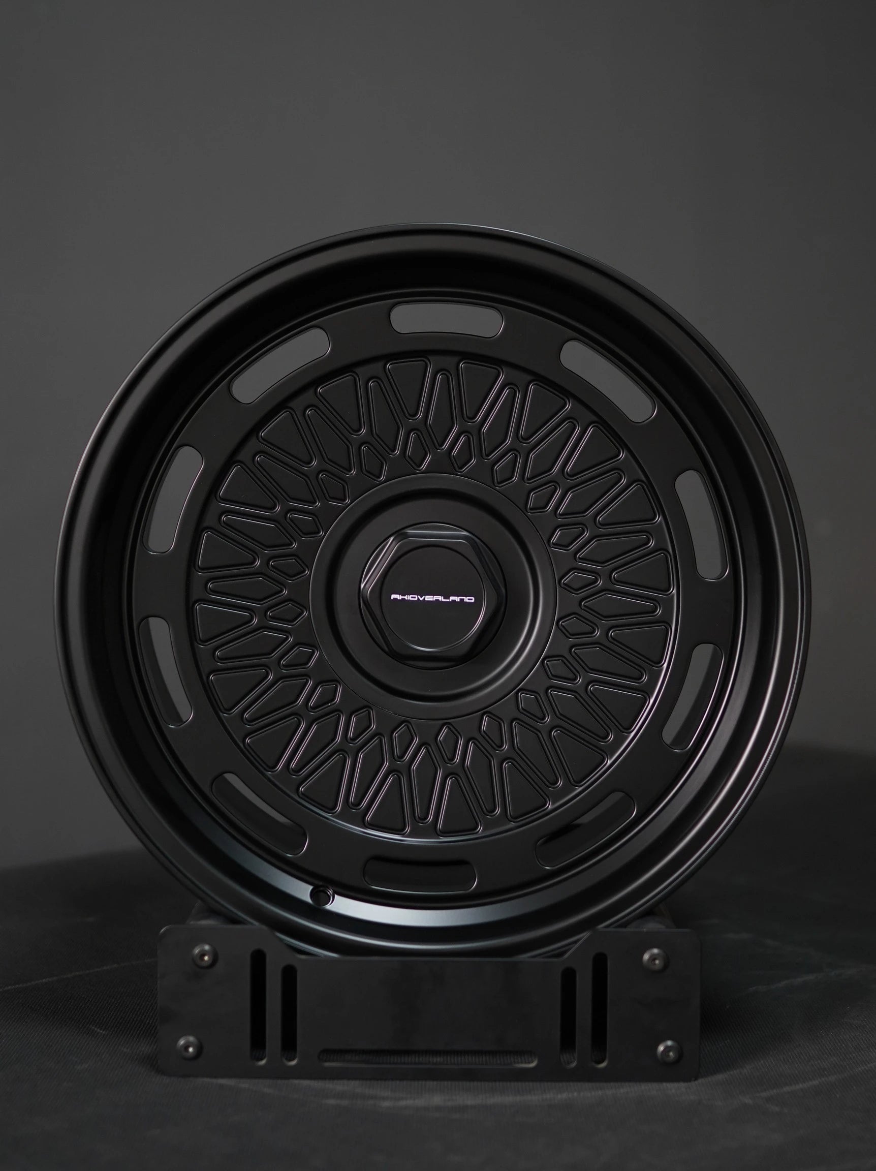 AkiOverland 5x130 mesh wheels in matte black shown front angle on display stand – Porsche offroad compatible.