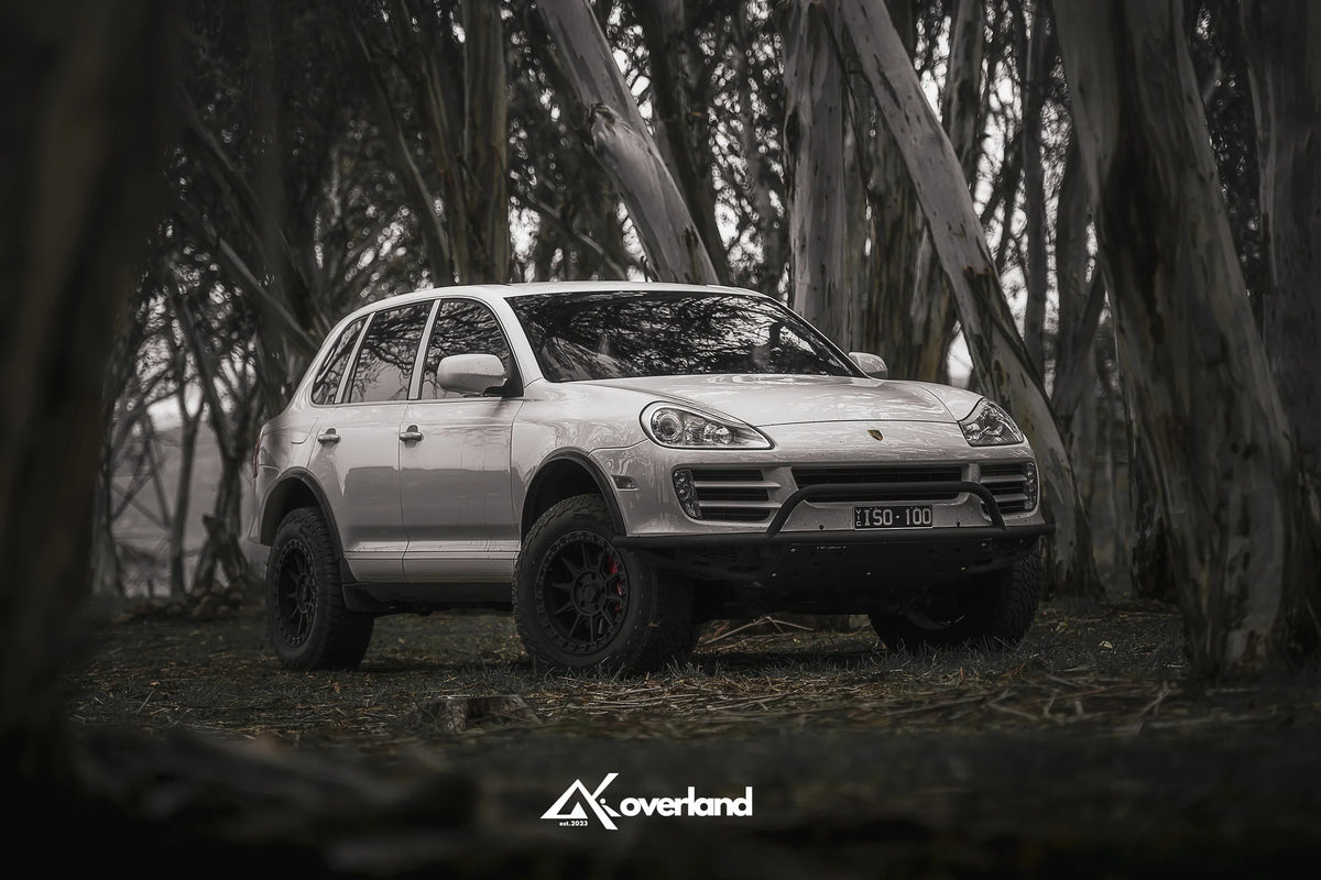 Porsche Cayenne 957 off-road stance with AkiOverland suspension lift, subframe drop and steel tubular bumper designed for winch installation.
