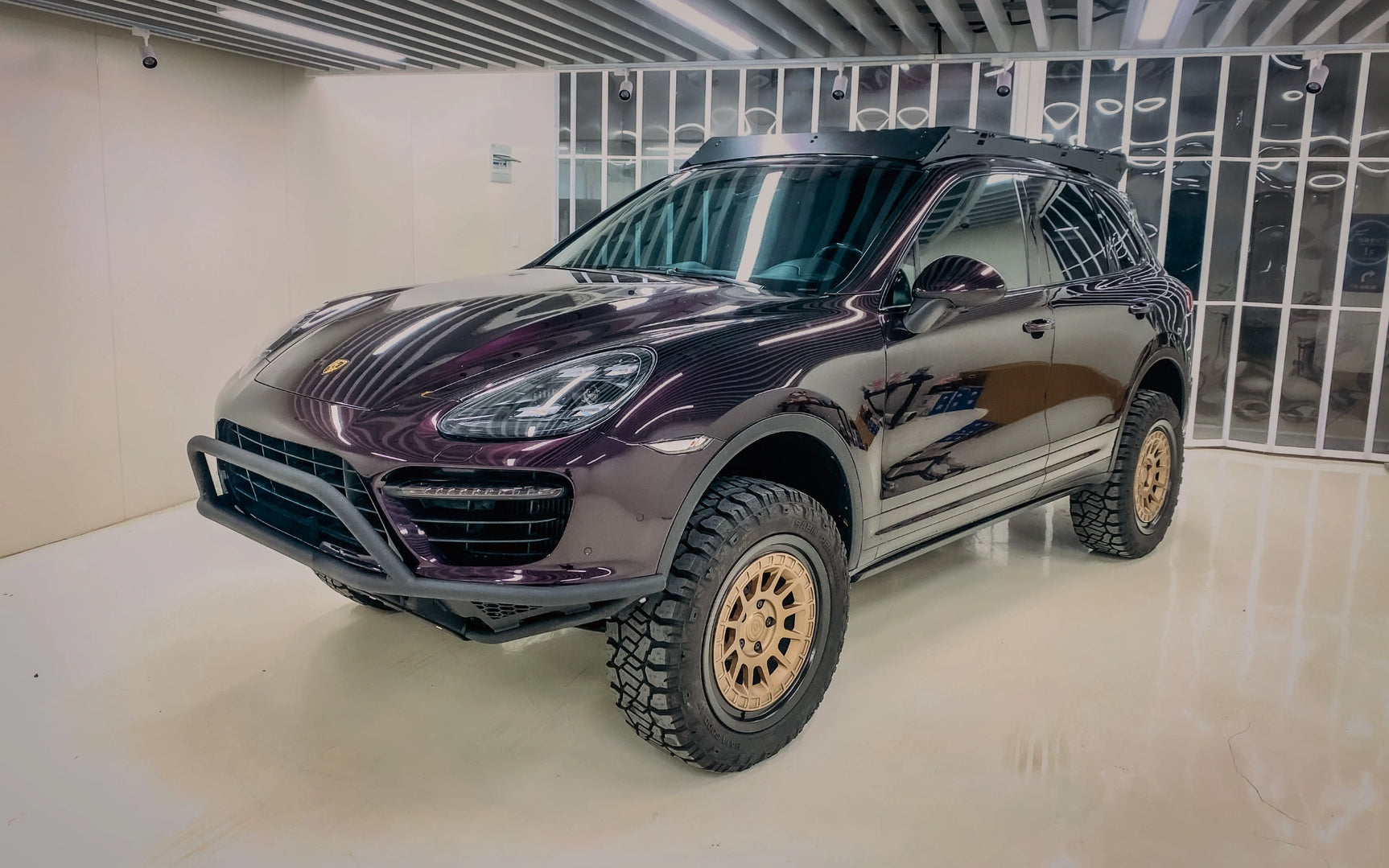 Akioverland Porsche Cayenne 958 lifted with off-road tires in a showroom setting