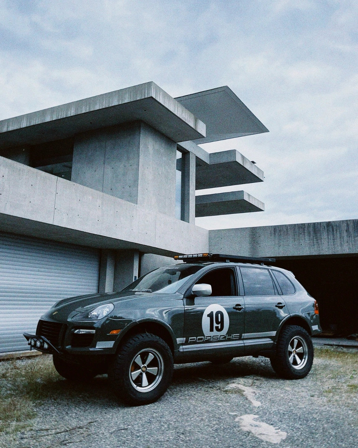 Porsche Cayenne 957 lifted on 5x130 wheels in front of modern concrete architecture.