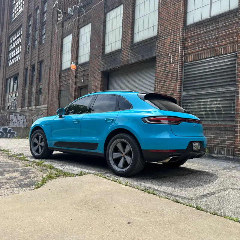 Rear three-quarter view of 2021 Porsche Macan Miami Blue Sully at Cleveland Ohio historic brick warehouse district with Terminal Tower in background — pre-AkiOverland x WrapWorkz Edition W build
