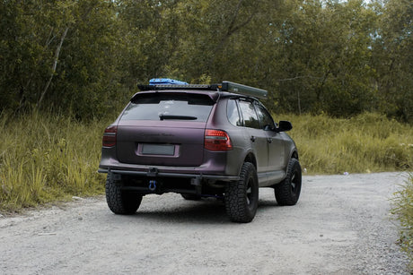 Purple Porsche Cayenne 957 overland with off-road tires and roof rack on a dirt road