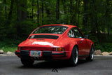 Rear view of red Porsche 911 SC G Body with custom Fuchs Reimagined wheels in forest setting