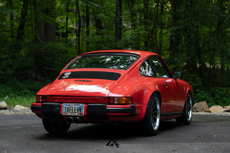 Rear view of red Porsche 911 SC G Body with custom Fuchs Reimagined wheels in forest setting