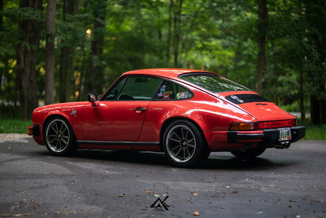 Red 1982 Porsche 911 SC parked in the woods with 5x130 forged Fuchs-style custom wheels