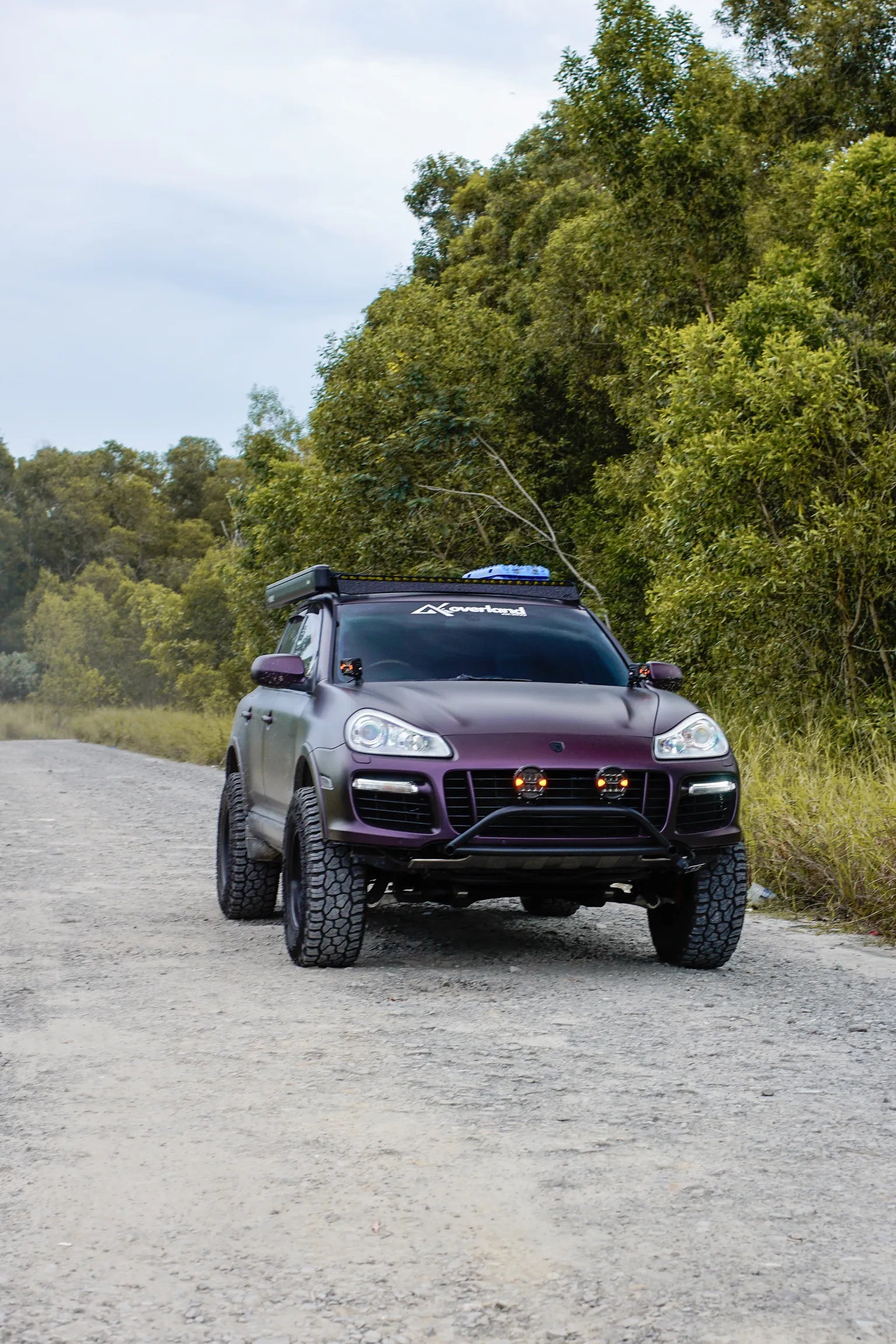 Luxury SUV Porsche Cayenne 957 overland lifted on a gravel road with trees in the background