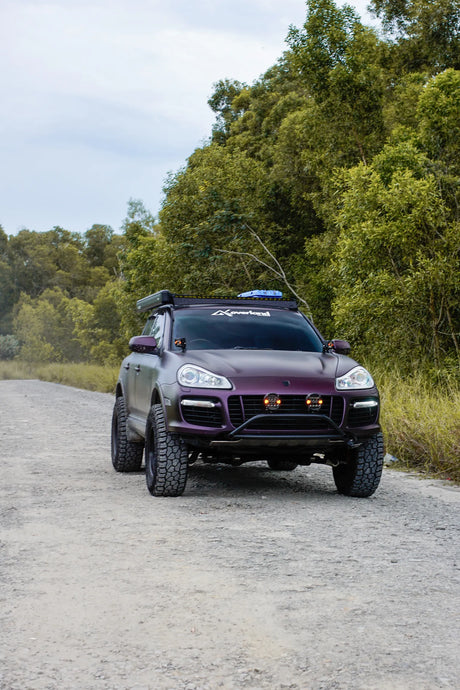 Luxury SUV Porsche Cayenne 957 overland lifted on a gravel road with trees in the background