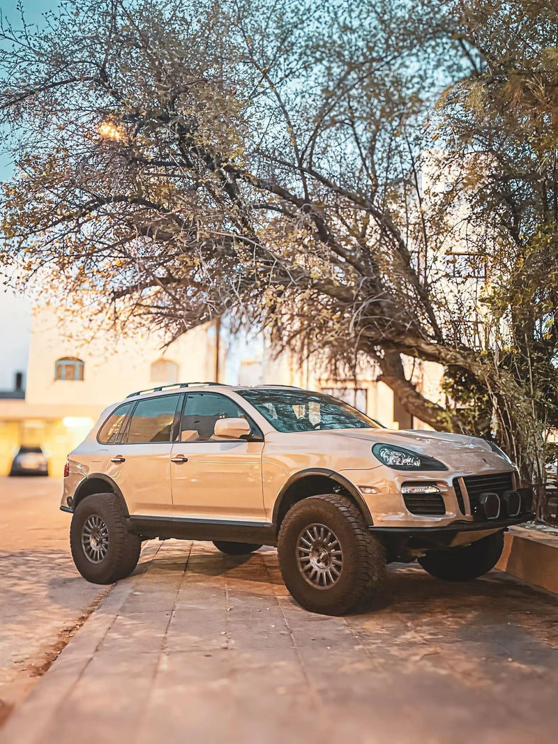 Sand colour Porsche cayenne parked on a driveway with trees and a house in the background in kuwait akioverland