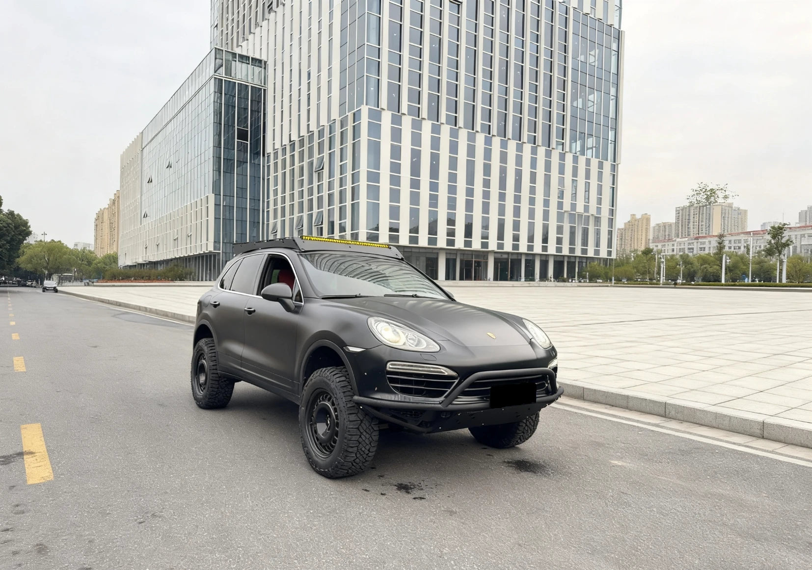 Porsche cayenne 958 matte black city street with modern buildings in the background