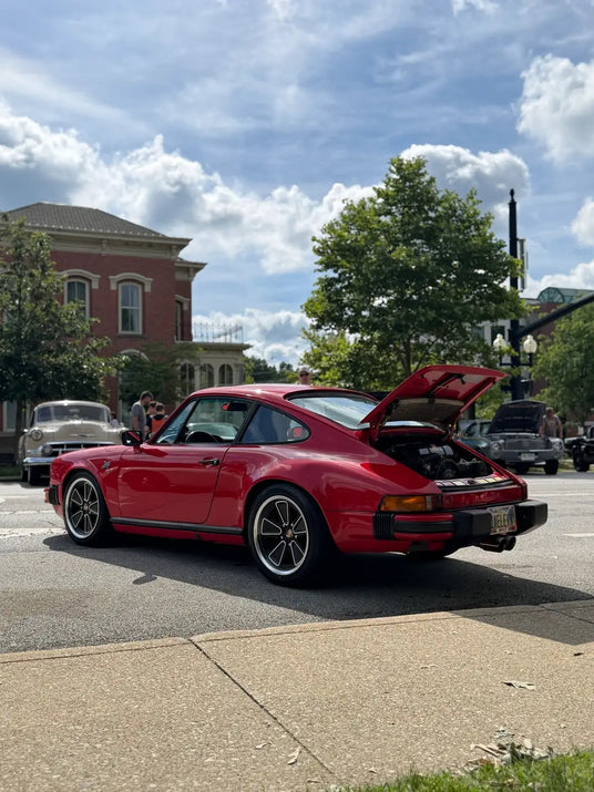 1982 Porsche 911 SC with rear engine lid open and AkiOverland 5x130 Fuchs Reimagined wheels on display at outdoor car show