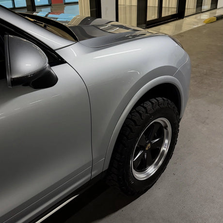 Silver Porsche Cayenne 958 with a lift and AkiOverland Classic Fuchs 5x130 wheels, machined lip and satin spokes, parked in a car park