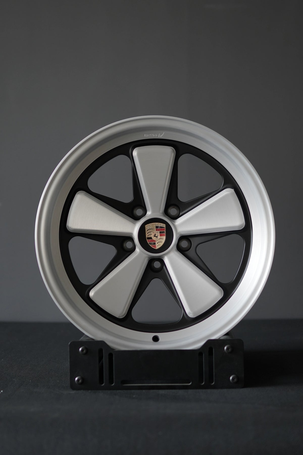AkiOverland Edition W forged Fuchs-style wheel in 5x130 Porsche fitment, studio-mounted on a display stand