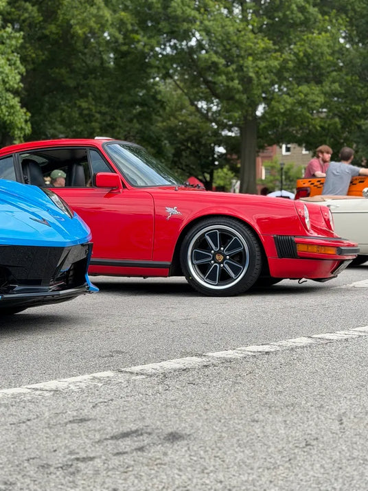 Low side angle of 1982 Porsche 911 SC showing AkiOverland 5x130 Fuchs Reimagined wheel detail alongside modern Porsche 992