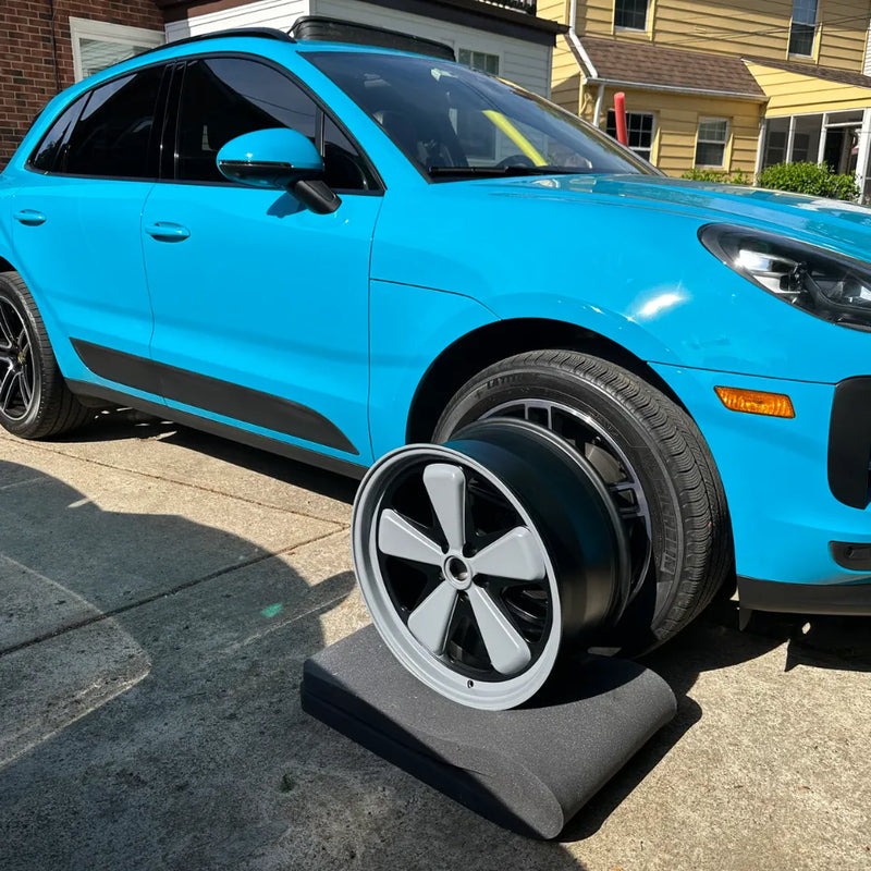 AkiOverland x WrapWorkz Edition W Forged Fuchs wheel held in front of 2021 Porsche Macan Miami Blue Sully in Cleveland Ohio driveway — crayon grey satin black two-tone forged wheel reveal before fitment