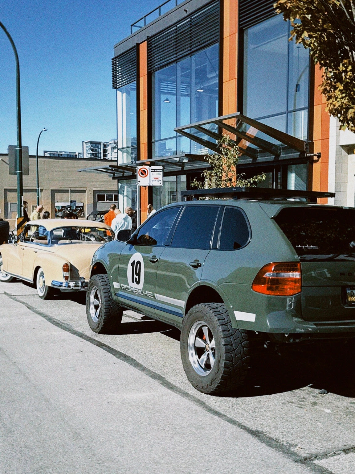 Porsche Cayenne 957 off-road build with 5x130 wheels parked behind sports car outside modern building.