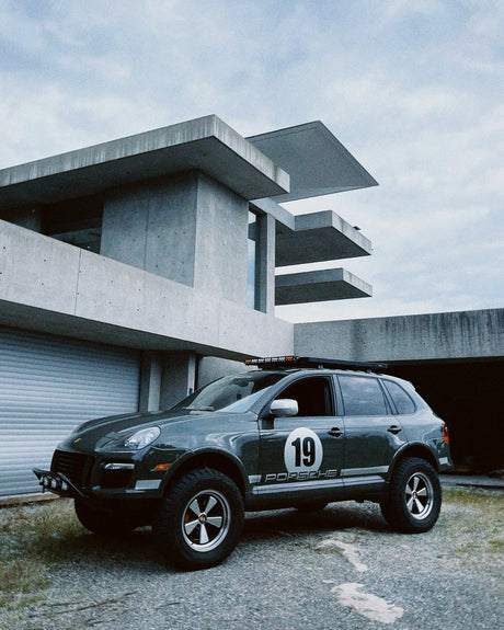 Porsche Cayenne 957 lifted on 5x130 wheels in front of modern concrete architecture.