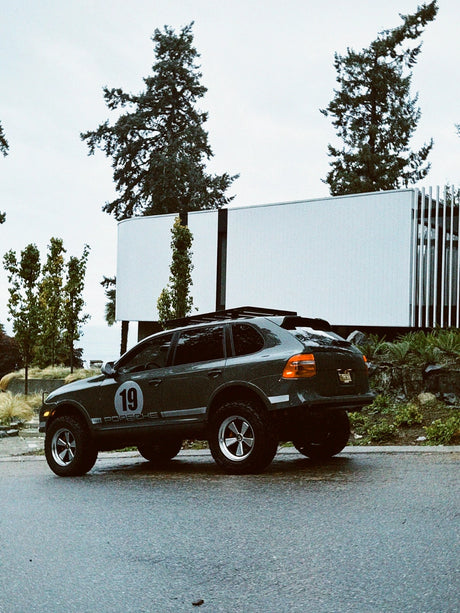 Cayenne 957 off-road build parked near  modern building showing Akioverland lift kit and wheels