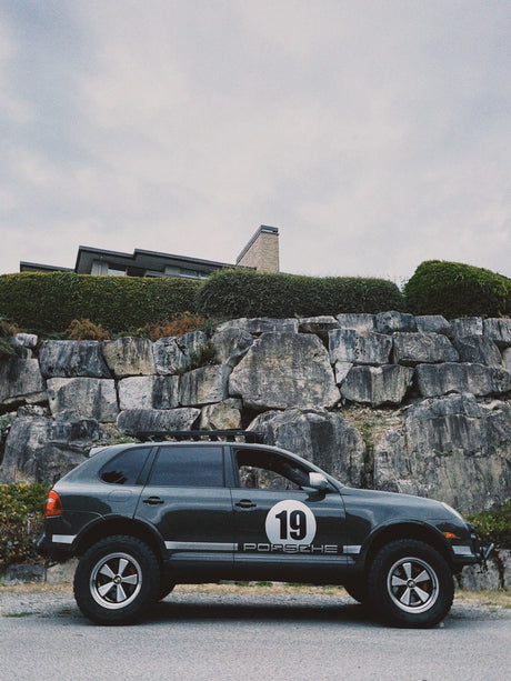 Porsche Cayenne 957 with 5x130 wheels and rally number 19 decal parked in rocky background