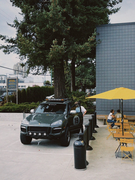 Off-road Porsche Cayenne 957 on AkiOverland Edition W 5x130 wheels parked near an outdoor cafe and urban plaza