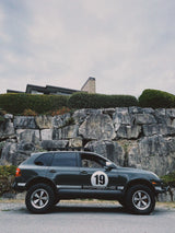 Rally number 19 Porsche Cayenne 957 on AkiOverland Edition W 5x130 forged wheels against a rocky background