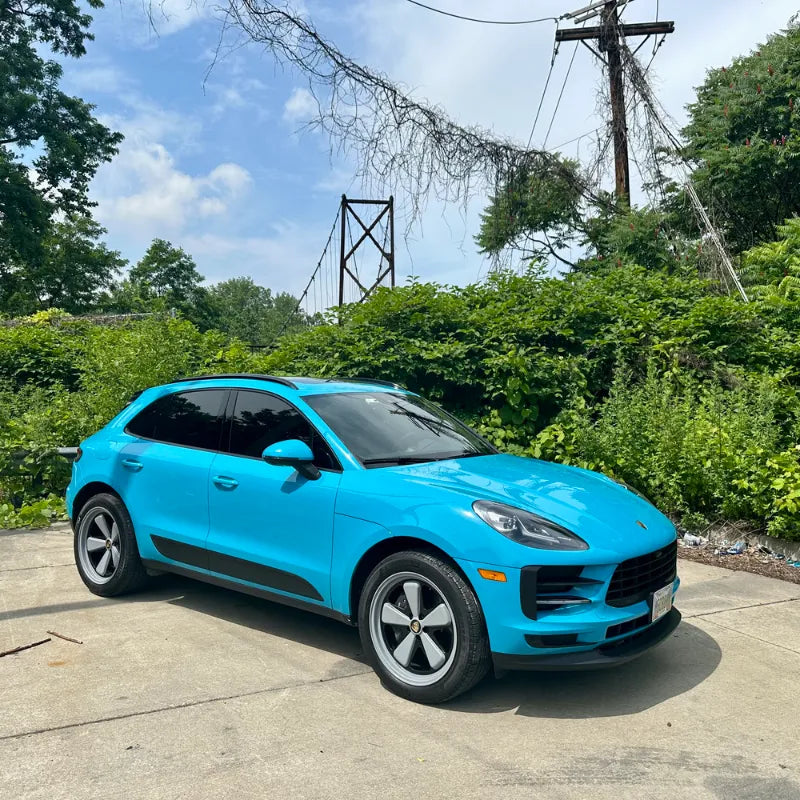 Front three-quarter view of 2021 Porsche Macan Miami Blue Sully near Cleveland Ohio suspension bridge surrounded by summer greenery — pre-Edition W Forged Fuchs wheel build stage