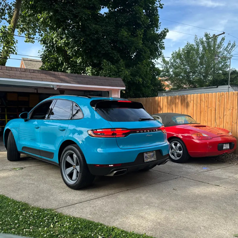 Rear view of 2021 Porsche Macan Miami Blue Sully alongside red Porsche Boxster in Cleveland Ohio home driveway — pre-AkiOverland x WrapWorkz Edition W Forged Fuchs wheel build, Cuyahoga County