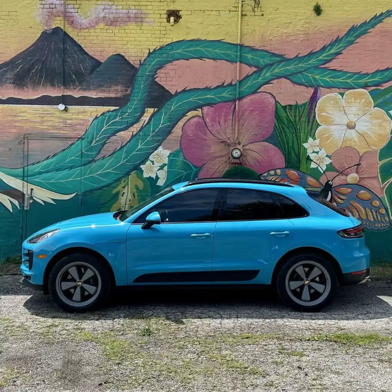 Full side profile of 2021 Porsche Macan Miami Blue against Cleveland Ohio tropical floral street mural — pre-AkiOverland Edition W Forged Fuchs wheel build stage