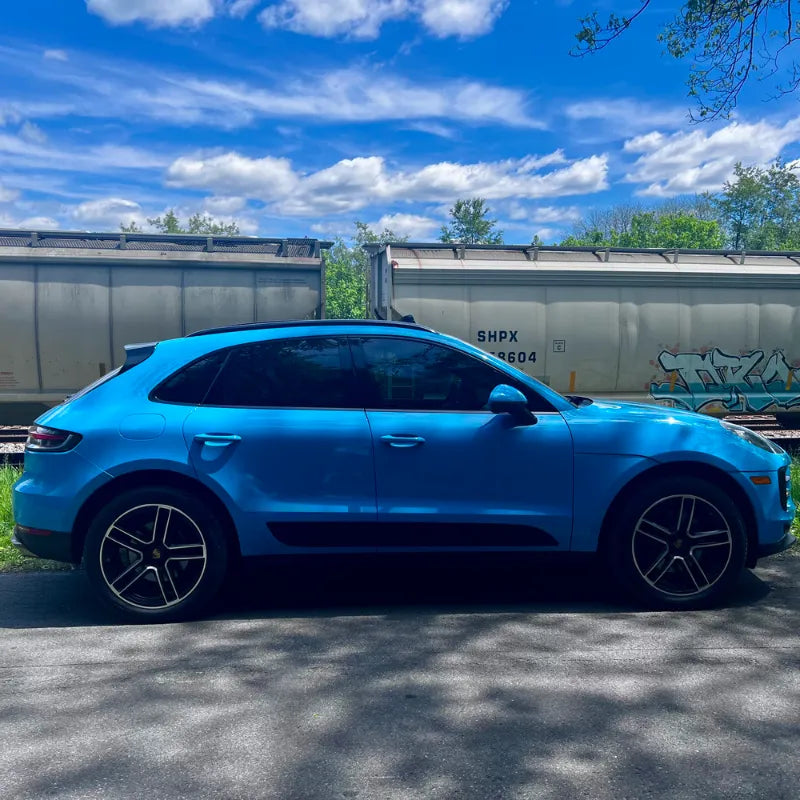Full side profile of 2021 Porsche Macan Miami Blue Sully parked alongside freight train in Cleveland Ohio 