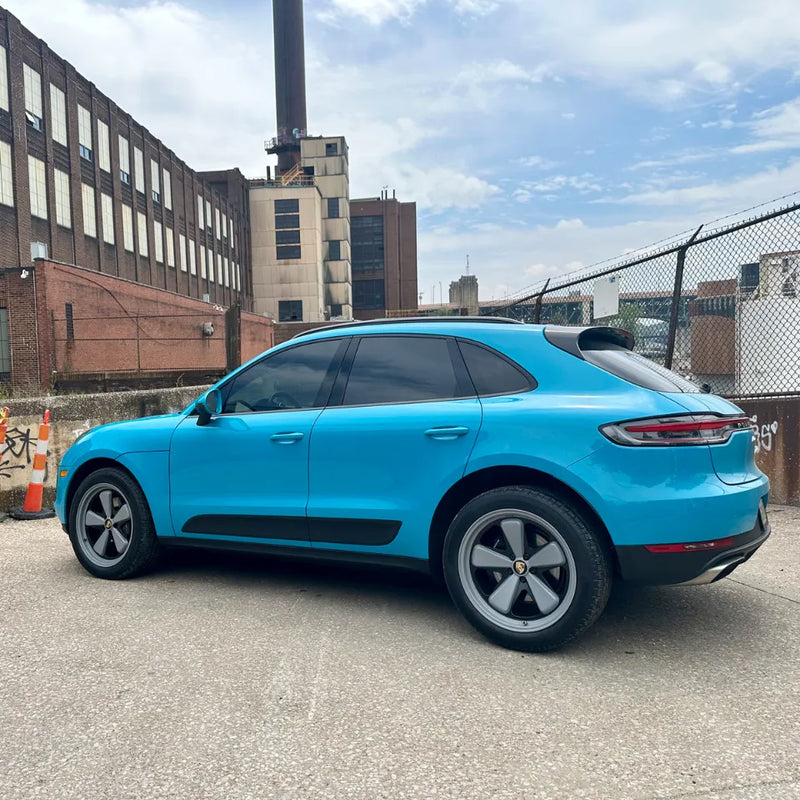 Full side profile of 2021 Porsche Macan Miami Blue Sully at Cleveland Ohio industrial district with brick factory building and chimney stack — pre-AkiOverland x WrapWorkz Edition W Forged Fuchs wheel build