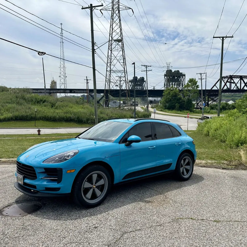  Front three-quarter view of 2021 Porsche Macan Miami Blue Sully at Cleveland Ohio industrial waterfront with power transmission towers and rail bridge — pre-Edition W Forged Fuchs build stage
