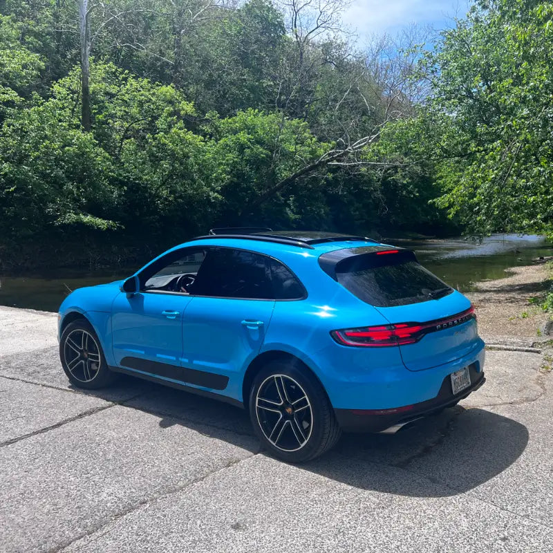 Rear three-quarter view of 2021 Porsche Macan Miami Blue Sully beside Cuyahoga River greenery in Cleveland Ohio