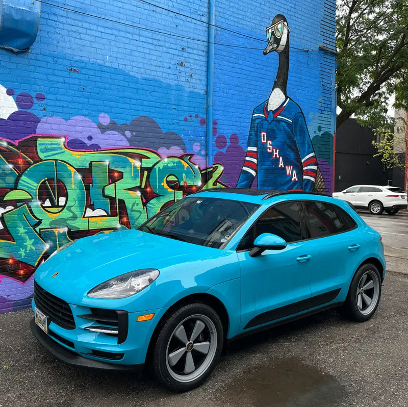 Front three-quarter view of 2021 Porsche Macan Miami Blue Sully on a rainy day outside Oshawa Ontario goose street mural — pre-AkiOverland x WrapWorkz Edition W Forged Fuchs wheel build