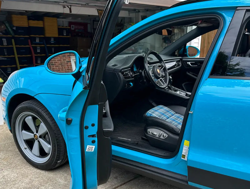  Driver door open on 2021 Porsche Macan Miami Blue Sully in Cleveland Ohio garage showing Karo Madras plaid seat insert and stock wheel — mid-build stage before AkiOverland x WrapWorkz Edition W Forged Fuchs fitment